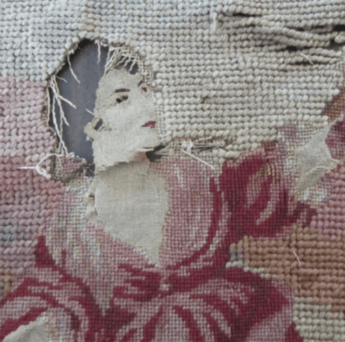 Embroidered scene depicting a woman in a red dress, with visible fabric loss and fraying around the head area.